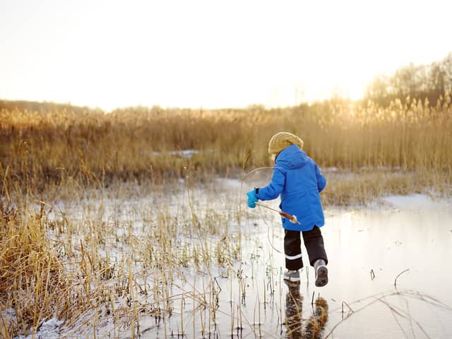 Preschool boy is playing on the ice of a frozen lake or river on a cold sunny winter sunset. Child sliding and having fun with during family hiking. Kids outdoor games in winter