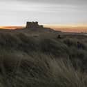 Children run through the sand dunes as the sun sets behind Bamburgh Castle