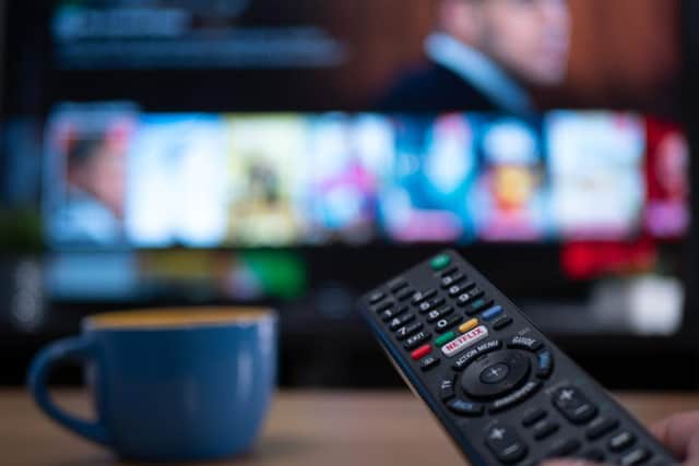 Netflix remote control with TV behind in evening with Netflix menu (Shutterstock)