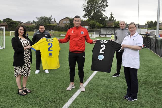 The back of Dunipace FC's new home and away strips for the 2021-2022 season feature Strathcarron Hospice and Maggie's Forth Valley logos respectively. Pictured: Cristina Pouso, Maggie's Forth Valley fundraising manager; John Marshall, club chairman; Danny Ashe, captain; Cameron Shanks, kitman; and Rozalja Glowacki, Strathcarron staff nurse. Picture: Michael Gillen.