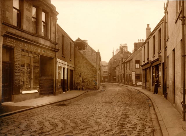 A view of Cow Wynd looking towards the High Street, with the long gone ironmongers shop Sime’s on the far left. The Wynd was originally just 13ft wide.