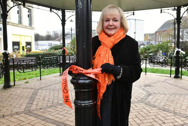 Fiona Richardson, president of Soroptimists International Falkirk ties an orange ribbon to one of the town centre lampposts.