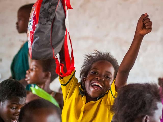 A child at a school in Malawi excitedly holds a bag from The Mary’s Meals Backpack Project.