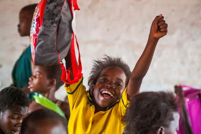 A child at a school in Malawi excitedly holds a bag from The Mary’s Meals Backpack Project.