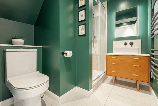 The gorgeous ground floor shower room boasts a drench head shower and handheld attachment while the teal walls, matt black tap and platinum grey towel radiator add a contemporary touch.