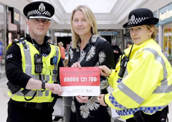 Suzanne Arkinson, manager Howgate Shopping Centre backs Police Scotland's campaign to end modern slavery by displaying poster in the centre with Inspector Chris Stewart and Constable Laura Christie